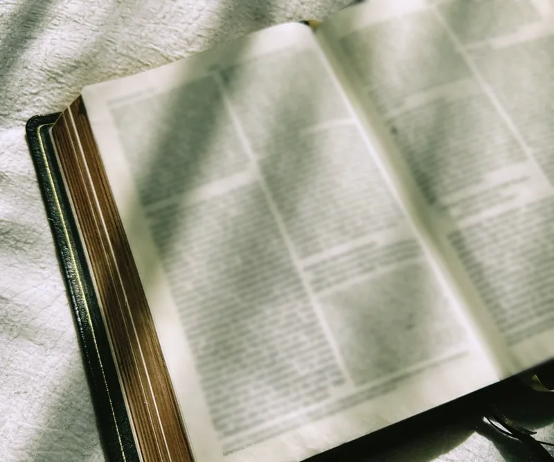 An open Bible lying on a white cloth in morning sunlight